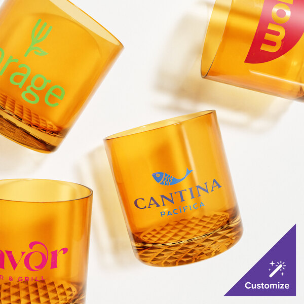A close-up of a Tossware amber plastic rocks glass with a logo.