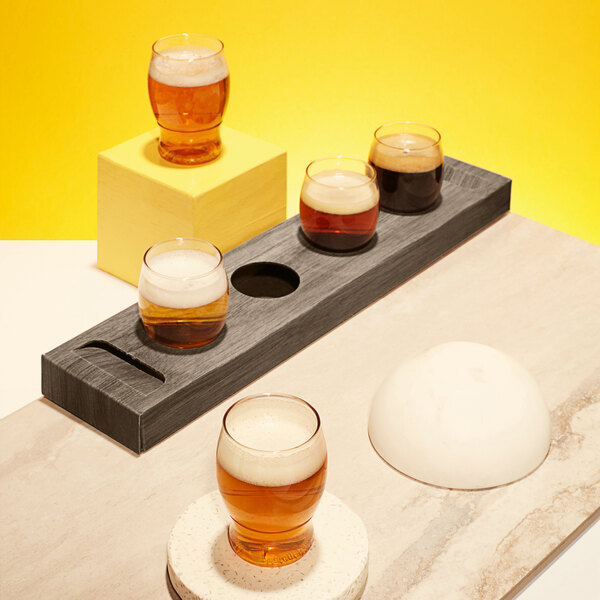 A Tossware cardboard tasting flight tray with several POP taster glasses of beer on a table.