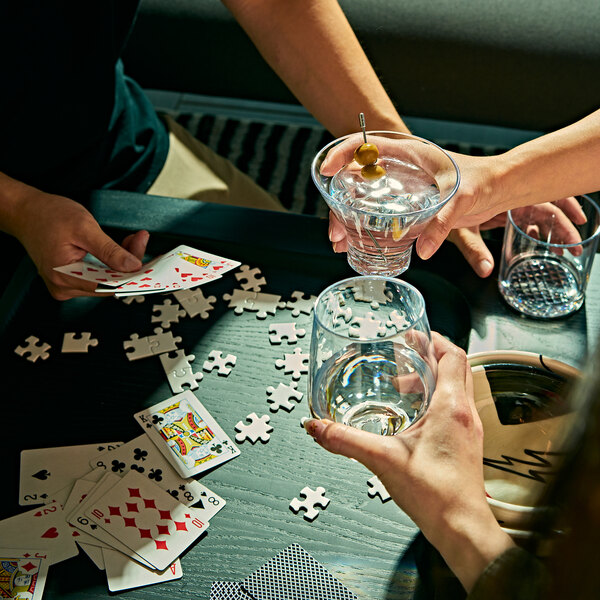 A hand holding a Tossware Tritan plastic stemless martini glass with olives in a drink.