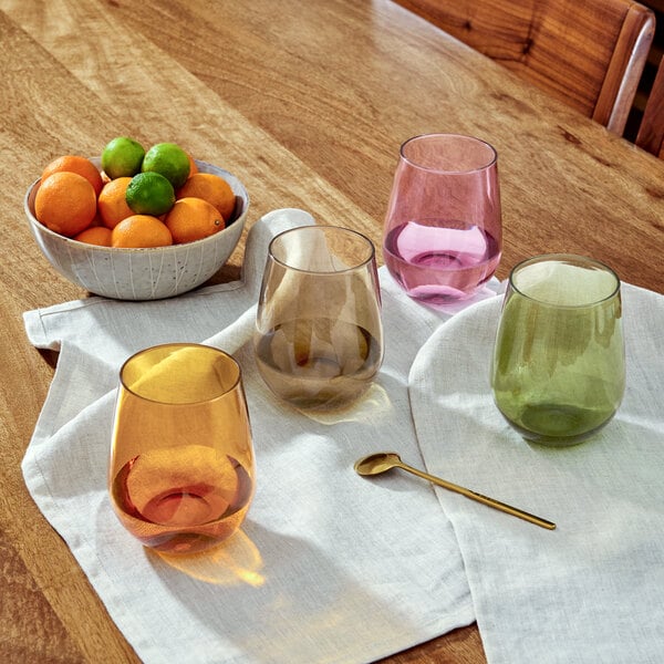 A table with a bowl of oranges and limes and stemless wine glasses filled with wine.