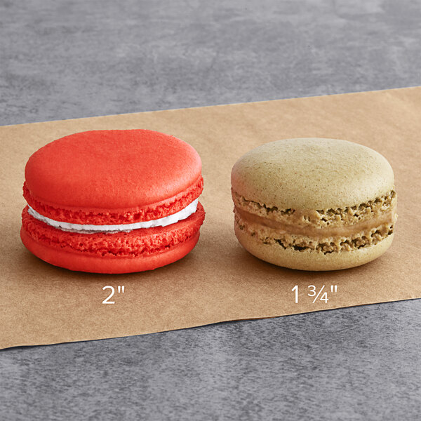 Two red macarons with white filling on brown paper.