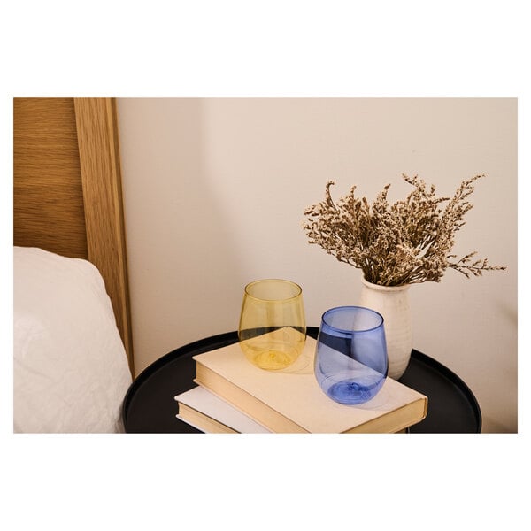 Two mint green Tossware Vino glasses on a table with a book and vase of dried flowers.