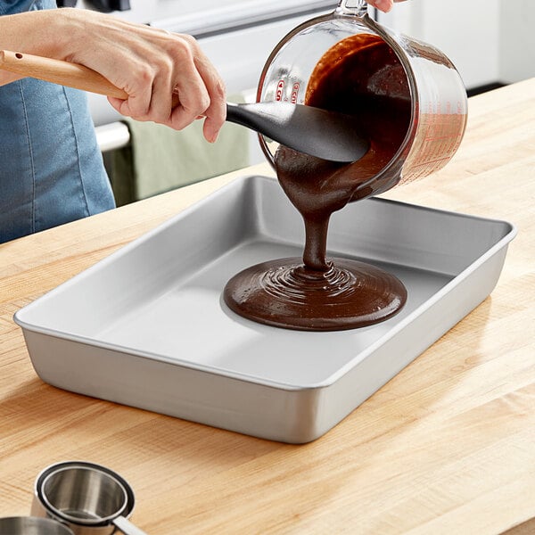 A woman pouring brown liquid into a Wilton rectangular cake pan.