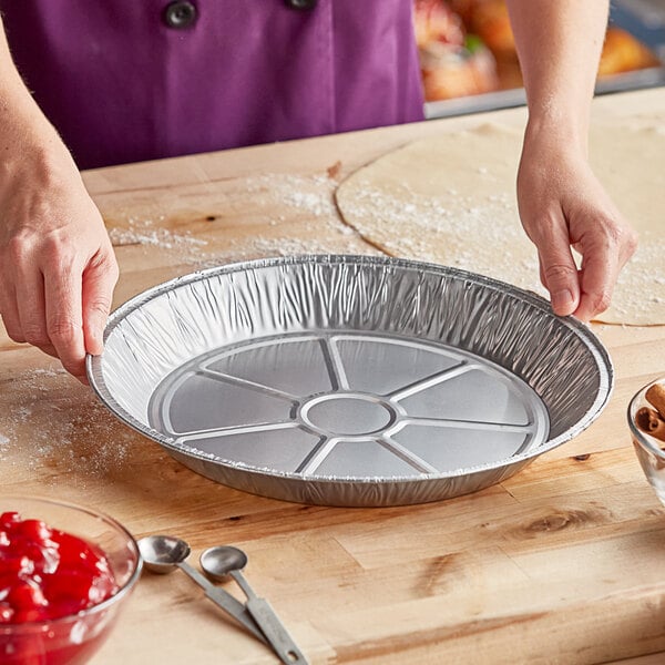 A woman in a purple coat using a Baker's Lane extra deep aluminum pie pan to prepare a pie.