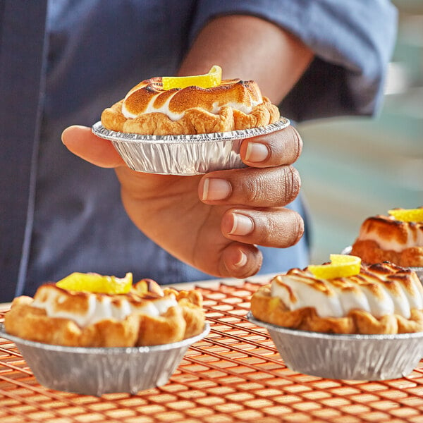 A person holding a tray of small pies in Baker's Lane foil tart pans.