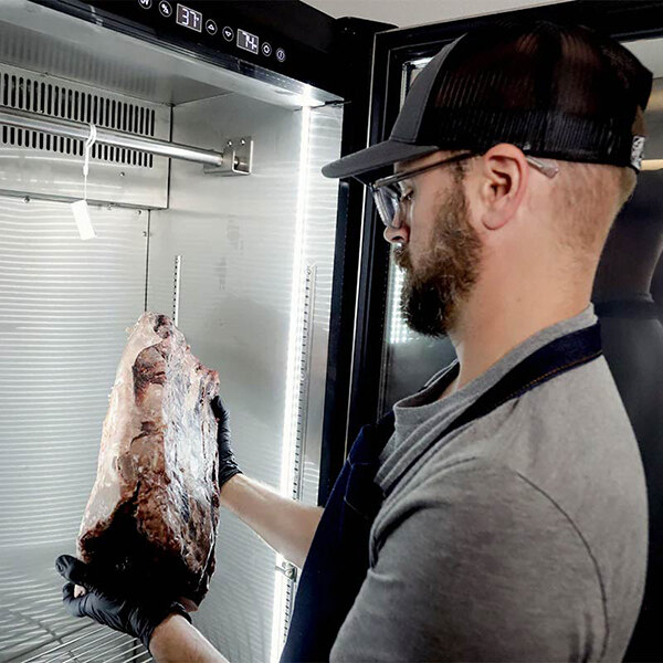 A man holding a large piece of meat in a Pro Smoker TR-300 Reserve dry aging cabinet.