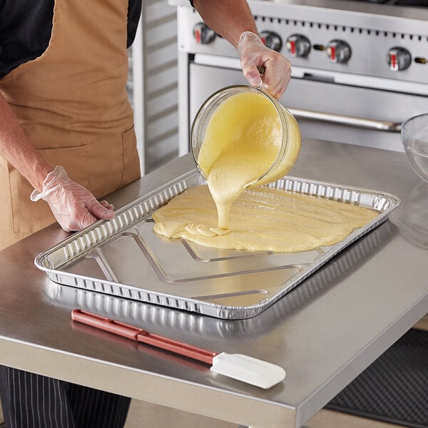 A person pouring yellow batter into a Baker's Mark foil cake pan.