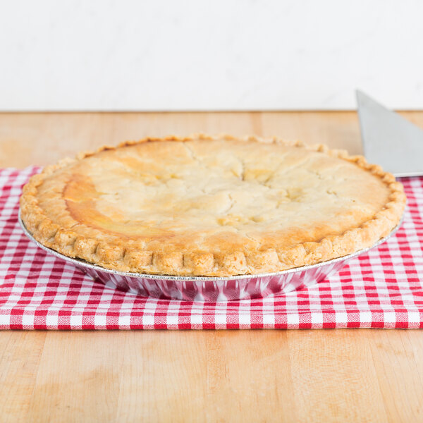 A pie in a Baker's Lane foil pie tin on a red and white checkered tablecloth.