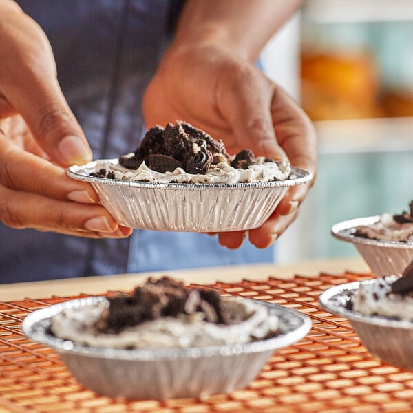 A person holding a Baker's Lane foil tart pan filled with food.