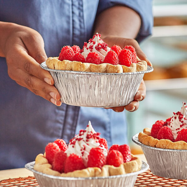 A woman holding a Baker's Lane foil pie pan filled with pies.