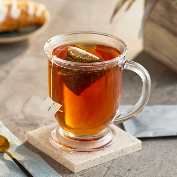 A glass cup of tea with a Dona Marrakesh Black Tea sachet in it.