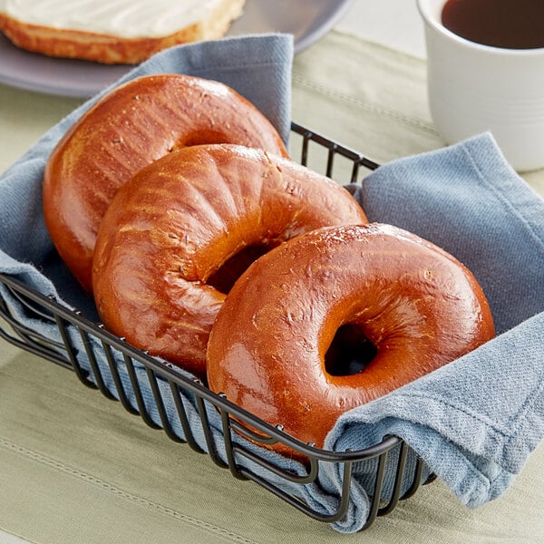 A basket of Just Bagels Pumpernickel Bagels on a table with a cup of coffee.