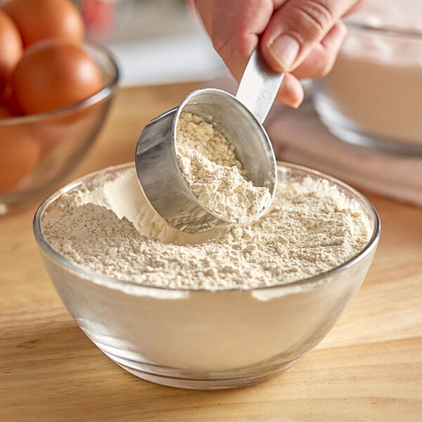 A person using a measuring spoon to scoop De Tulpen Vital Wheat Gluten into a bowl.