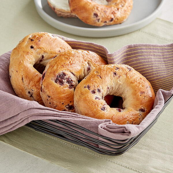 A basket of Just Bagels blueberry bagels on a table.