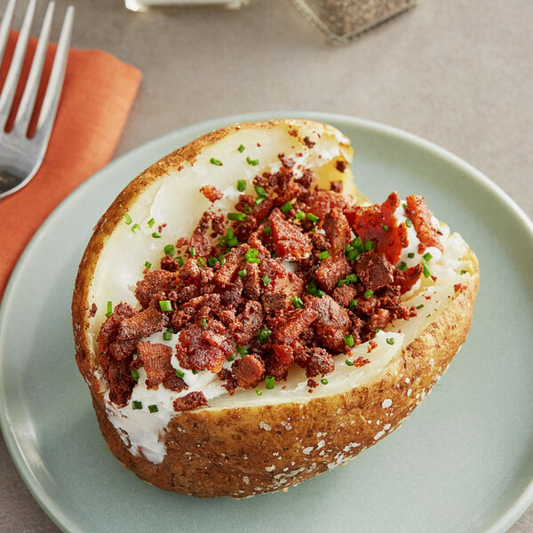 A baked potato with Thrilling Foods Plant-Based Vegan Bakon Bits and green onions on a plate.