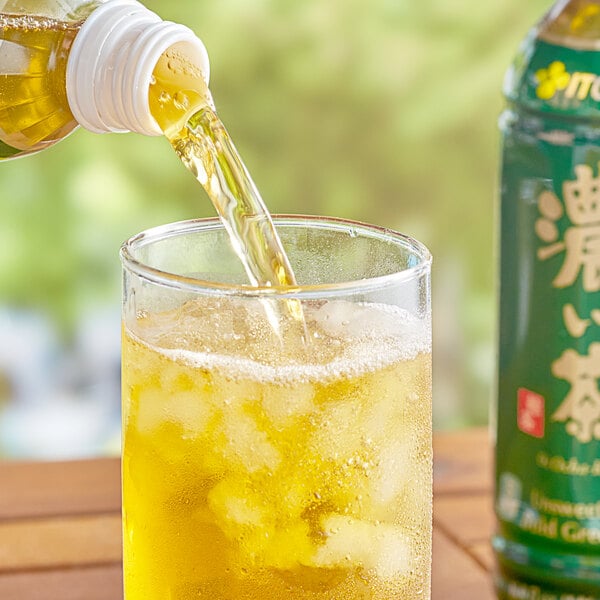 A person pouring Ito En Oi Ocha Koicha Bold Green Iced Tea into a glass of ice.