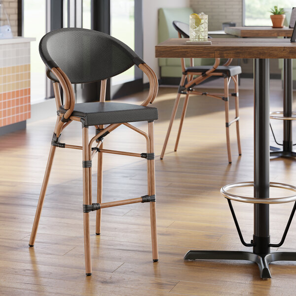 A black outdoor arm barstool with a woven seat and back, and light brown legs.
