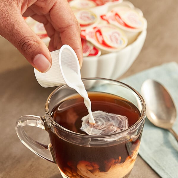 A person pouring Nestle Coffee-Mate into a cup of coffee.