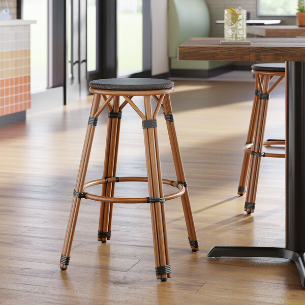 A backless barstool with a black seat and wooden legs, designed for outdoor use.