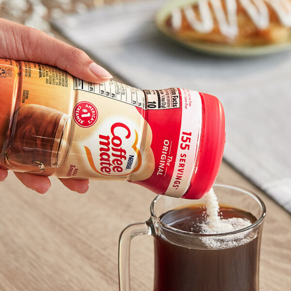 A hand pouring Nestle Coffee-Mate Original non-dairy coffee creamer into a glass of coffee.