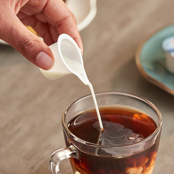 A hand holding a plastic cup of coffee with Nestle Coffee-Mate French Vanilla being poured into it.