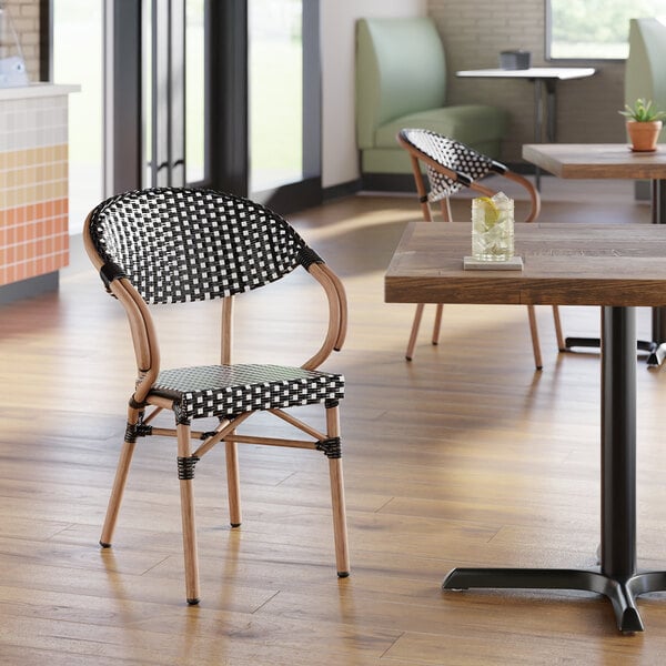 A black and white checkered weave rattan outdoor arm chair with a curved back and wooden-look frame.