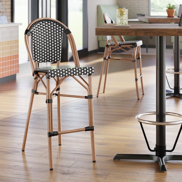 A black and white checkered weave rattan outdoor side barstool with a curved back and wooden legs.