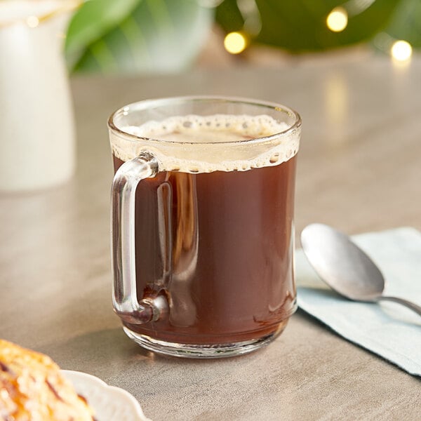 A glass mug of Nescafe Clasico instant coffee on a saucer with a spoon.