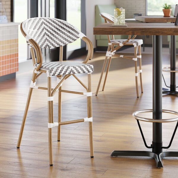 A rattan outdoor arm barstool with a gray and white chevron weave design.