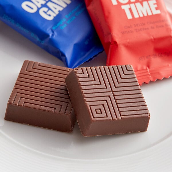 Two TCHO Oatally Awesome oat milk chocolate squares in blue wrappers on a plate.