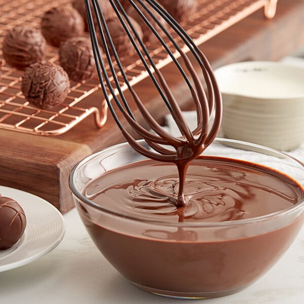 A bowl of TCHO Mighty Mosaic dark chocolate liquid with a whisk stirring it.