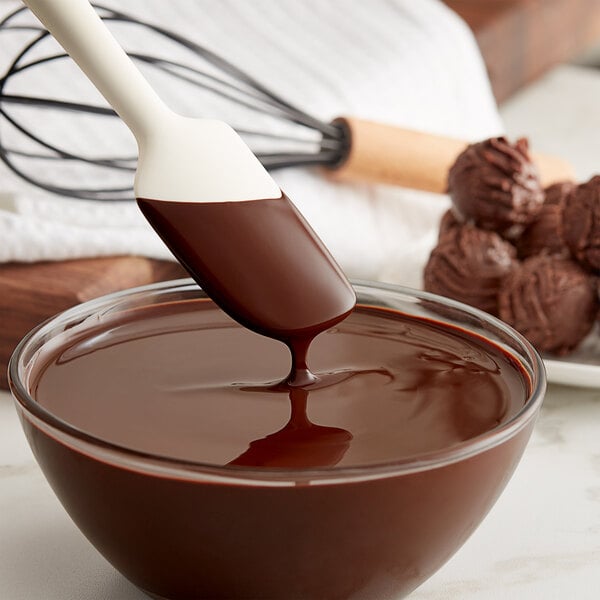 A bowl of TCHO Hella Dark chocolate sauce with a spoon stirring it.