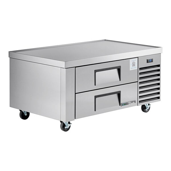 A stainless steel refrigerated chef base with two drawers and caster wheels.