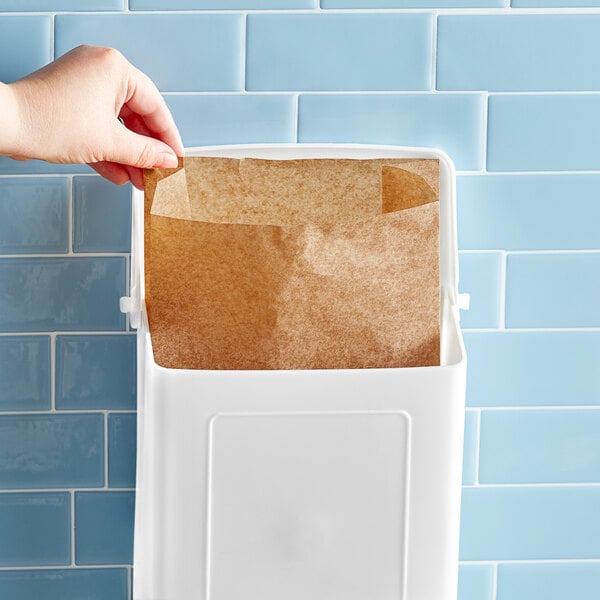 A hand putting a Lavex sanitary napkin receptacle bag in a white container.