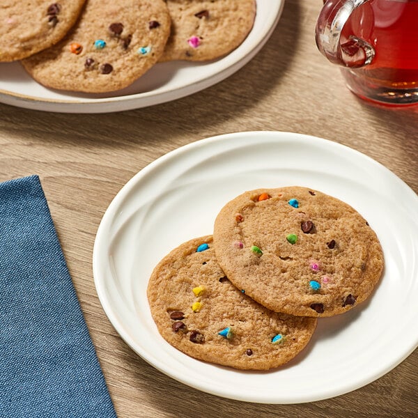 A plate of two Otis Spunkmeyer chocolate chip cookies on a table with a cup of tea.