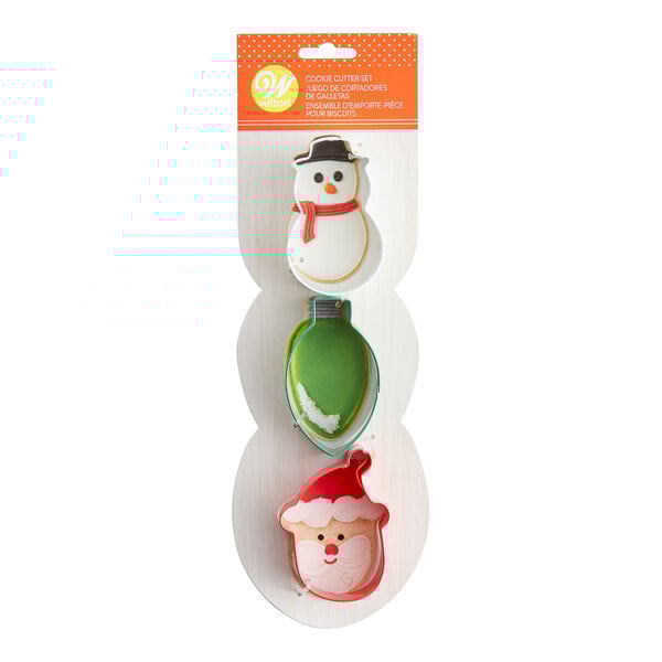 A package of three metal holiday cookie cutters shaped like a snowman, ornament, and tree.