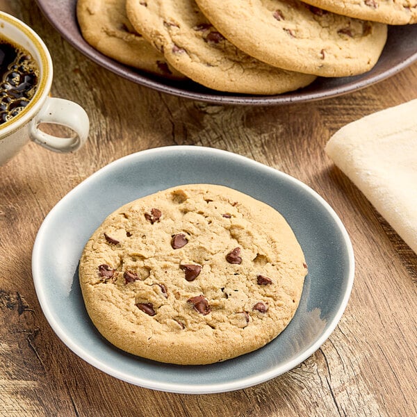 A plate of Otis Spunkmeyer chocolate chip cookies with a cup of coffee on a table.