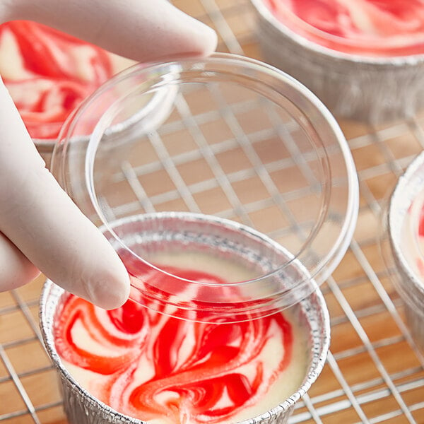 A hand putting a red and white swirl into a plastic container with a Baker's Lane lid.