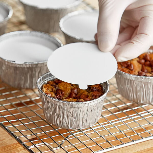 A hand putting a white lid on a Baker's Lane foil cup with food inside.