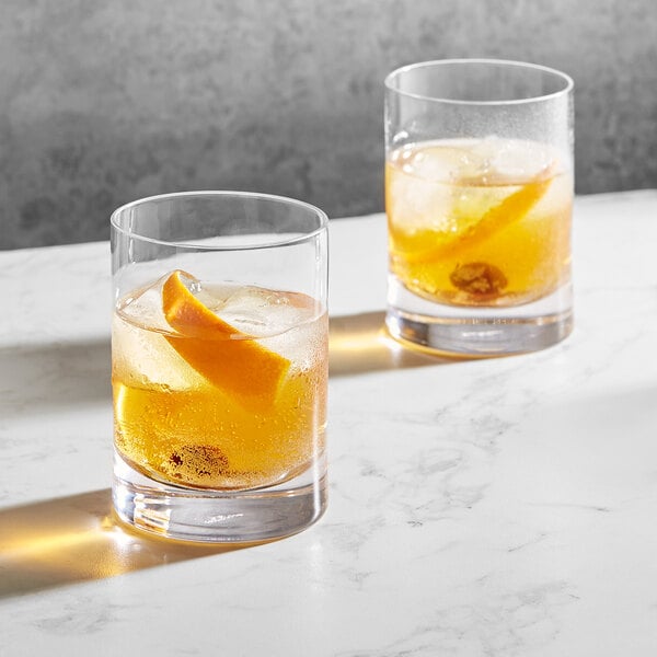 Two Della Luce Origins rocks glasses of whiskey with ice and orange slices.