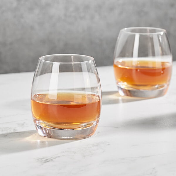 Two Della Luce Avalon Rocks glasses filled with brown liquid on a marble surface.