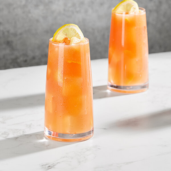 Two Della Luce Dion beverage glasses with orange liquid, lemon slices, and ice.