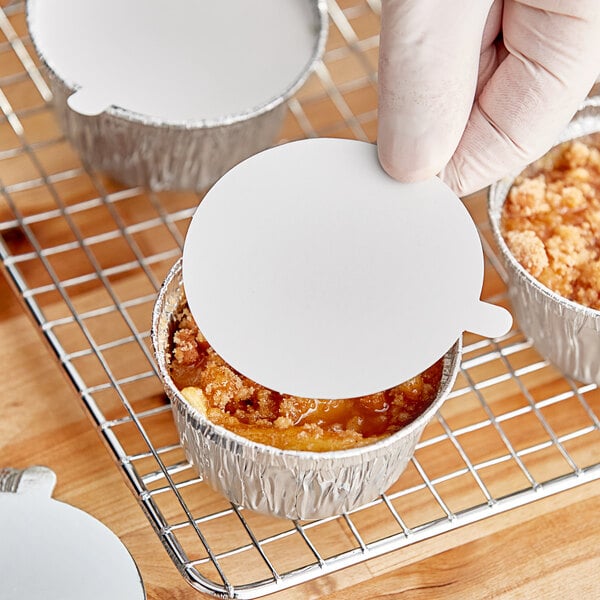 A hand holding a Baker's Lane round white paper lid over a small cup of food.