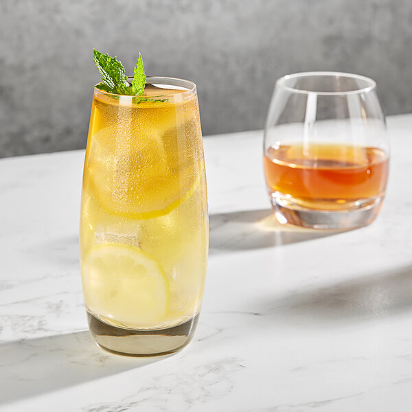 Two Della Luce Avalon Rocks glasses, one with brown liquid and ice, and one with lemonade, ice, and lemon slices.