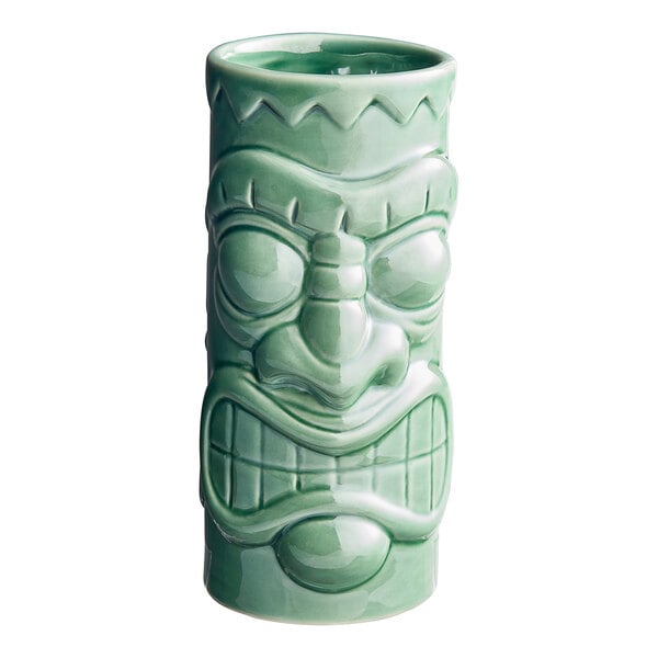 A close-up of a green ceramic Acopa Tiki Mug with a face carved on it.