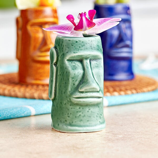 An Acopa green ceramic Tiki shot glass with a pink flower in it.