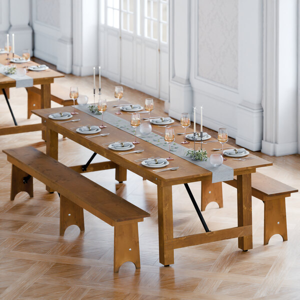 A Lancaster Table & Seating Vineyard Series long wooden table with two wooden benches set up outside with plates and glasses.