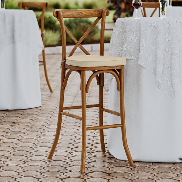 A Lancaster Table & Seating Vineyard Series Barrel Brown outdoor cross back bar stool with a Chardonnay tan cushion.