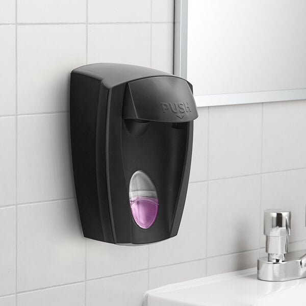 A black Kutol manual soap dispenser on a wall.