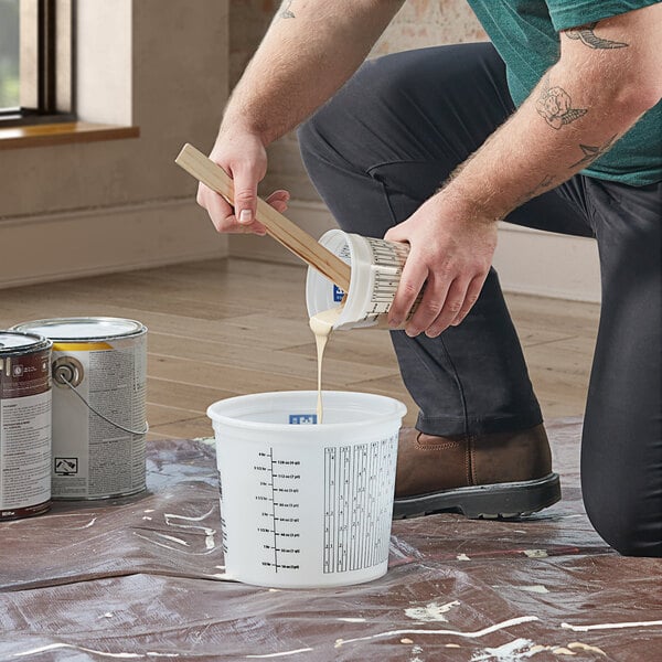 A man pouring white paint into a white Midwest Rake multi-purpose mixing container.